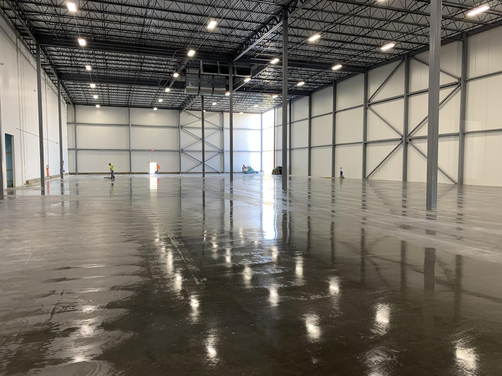 Completed freezer interior with insulated metal panel walls, exposed steel framing, and a freshly finished floor slab