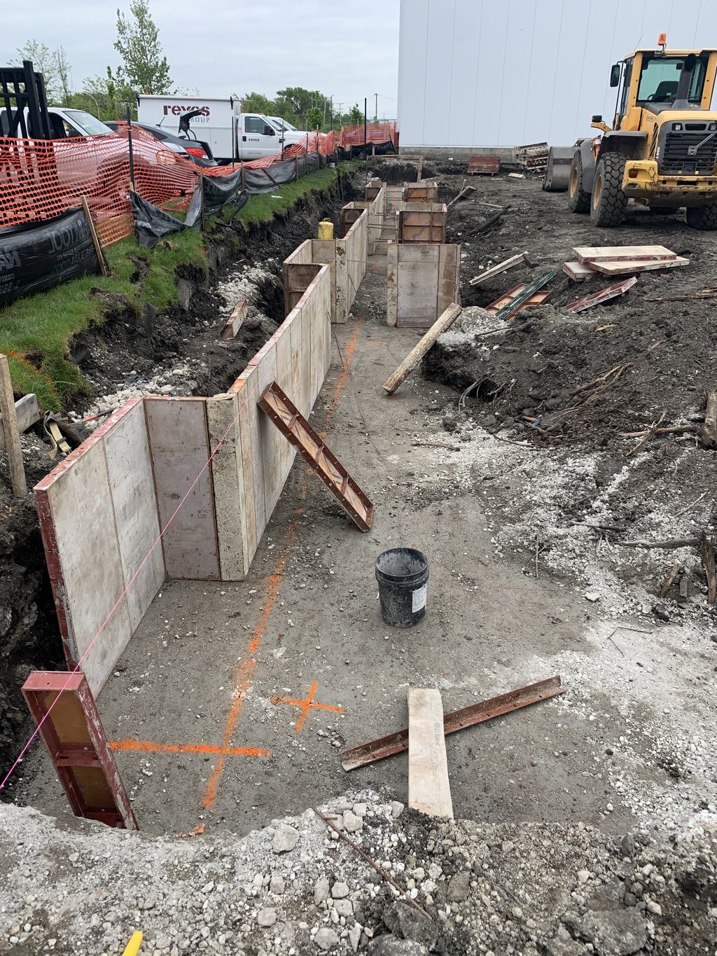 Formed concrete foundation walls and excavation at the freezer addition, with an excavator working in the background