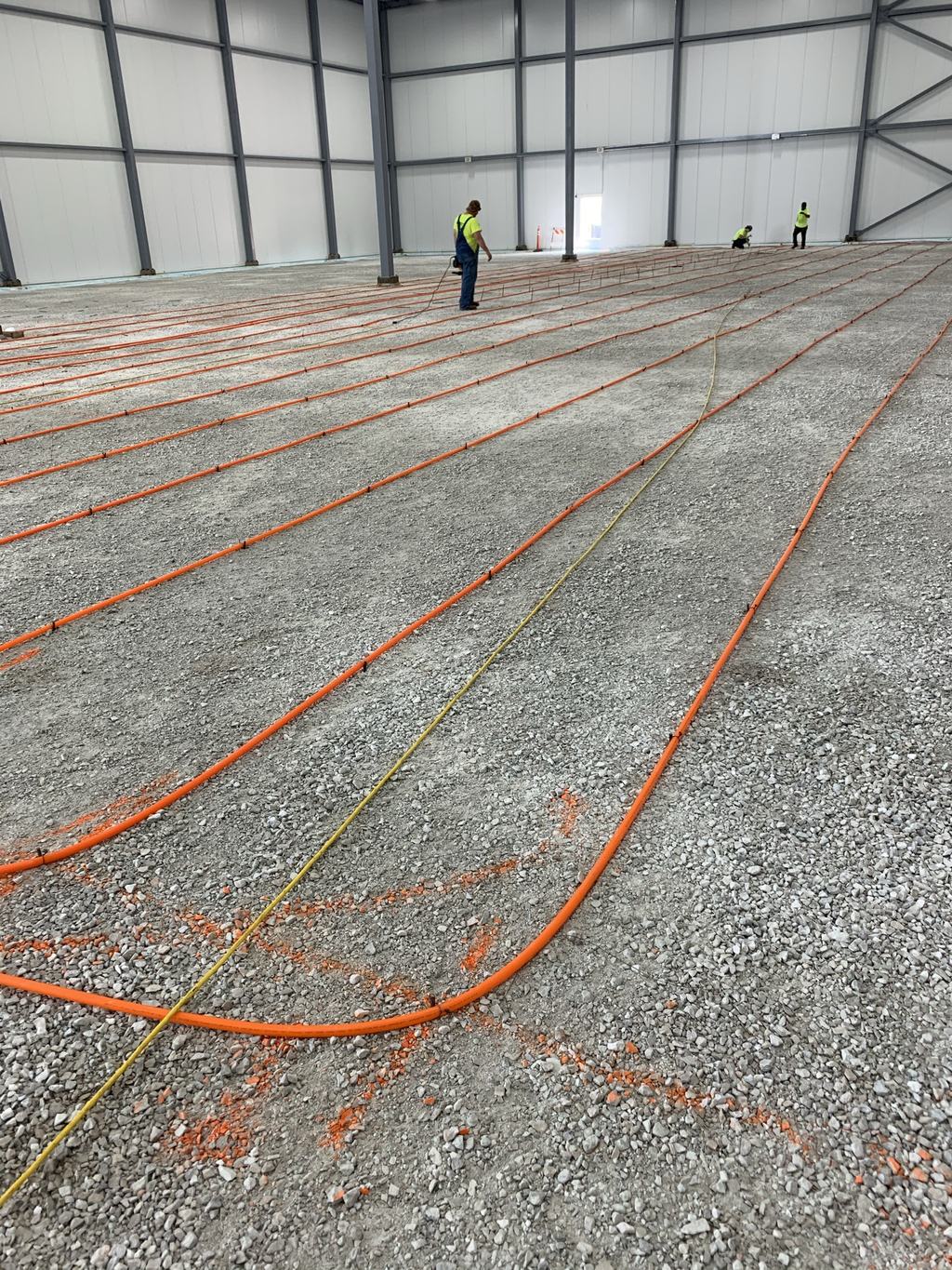 Orange glycol tubing run in loops across the stone base inside the insulated metal panel shell, ahead of the heated slab pour