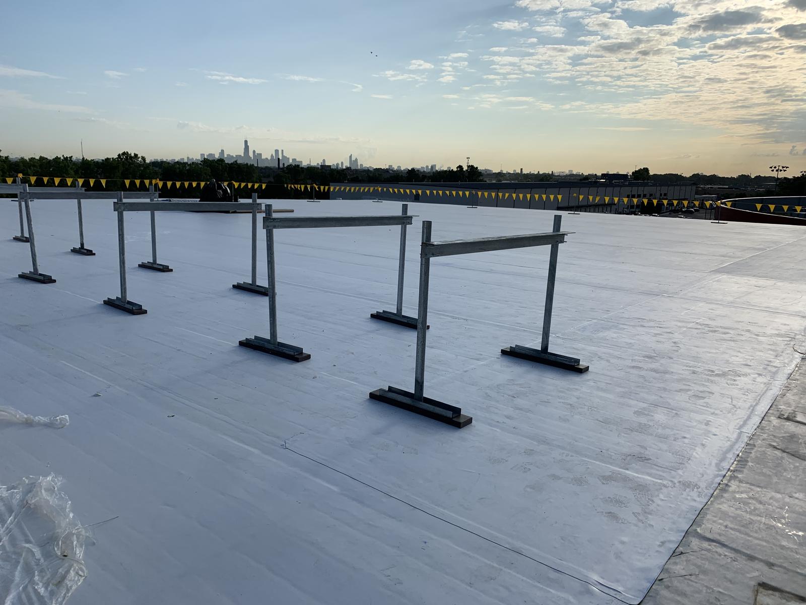 Rows of steel equipment supports set on the new roof membrane at dusk, with the Chicago skyline on the horizon
