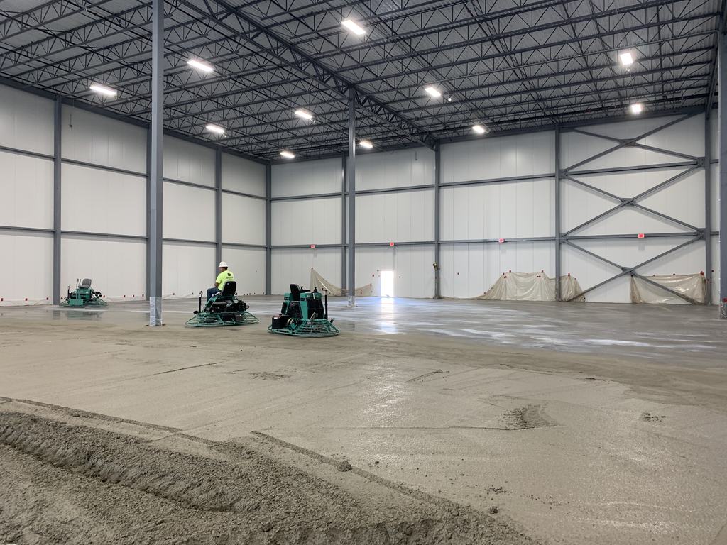 Two ride-on power trowels finishing the new concrete slab inside the freezer shell