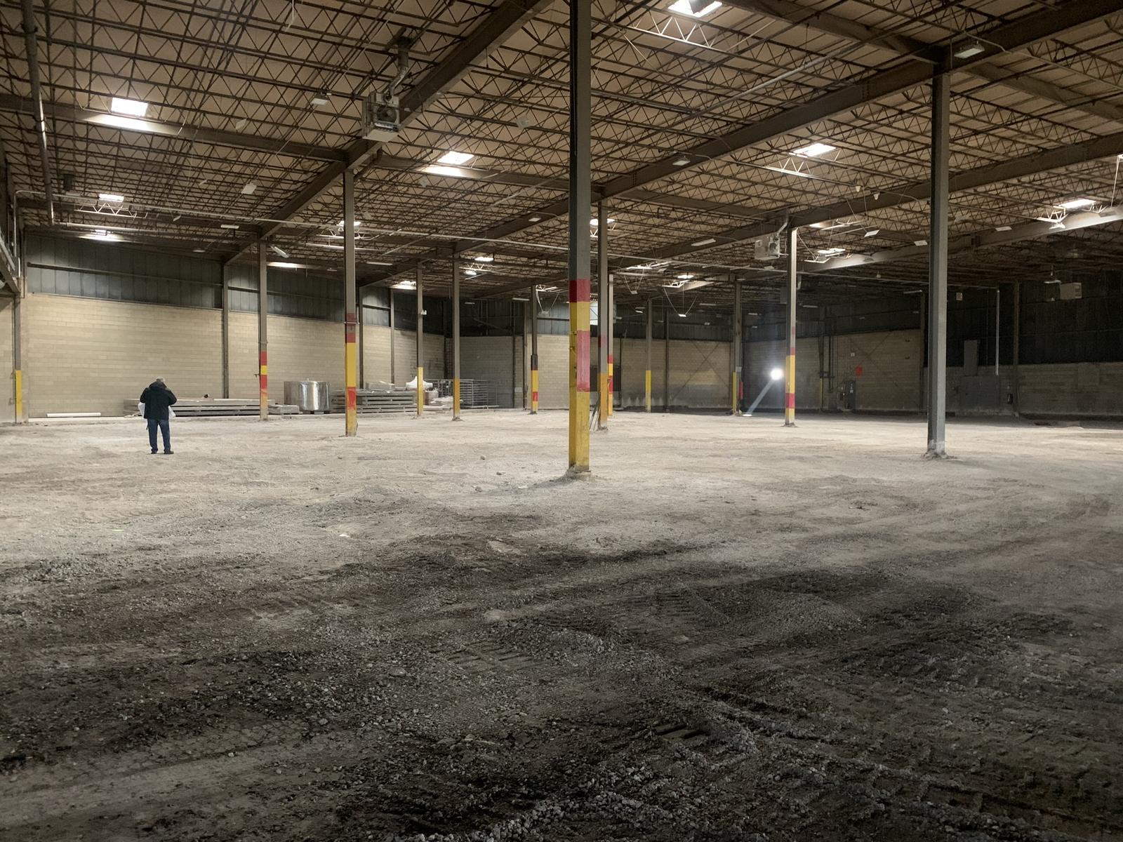 Interior of the plant stripped to subgrade during demolition, with the existing structural steel columns and roof deck exposed