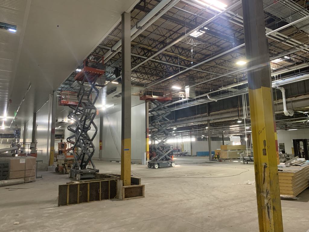Insulated metal panel wall and ceiling installation underway, with scissor lifts and stacked panels staged across the production floor