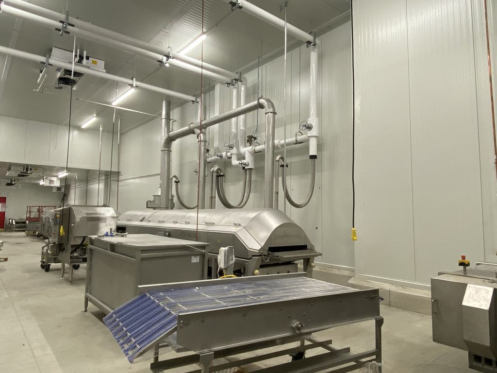 Stainless steel processing equipment set against new insulated metal panel walls, with overhead utility drops