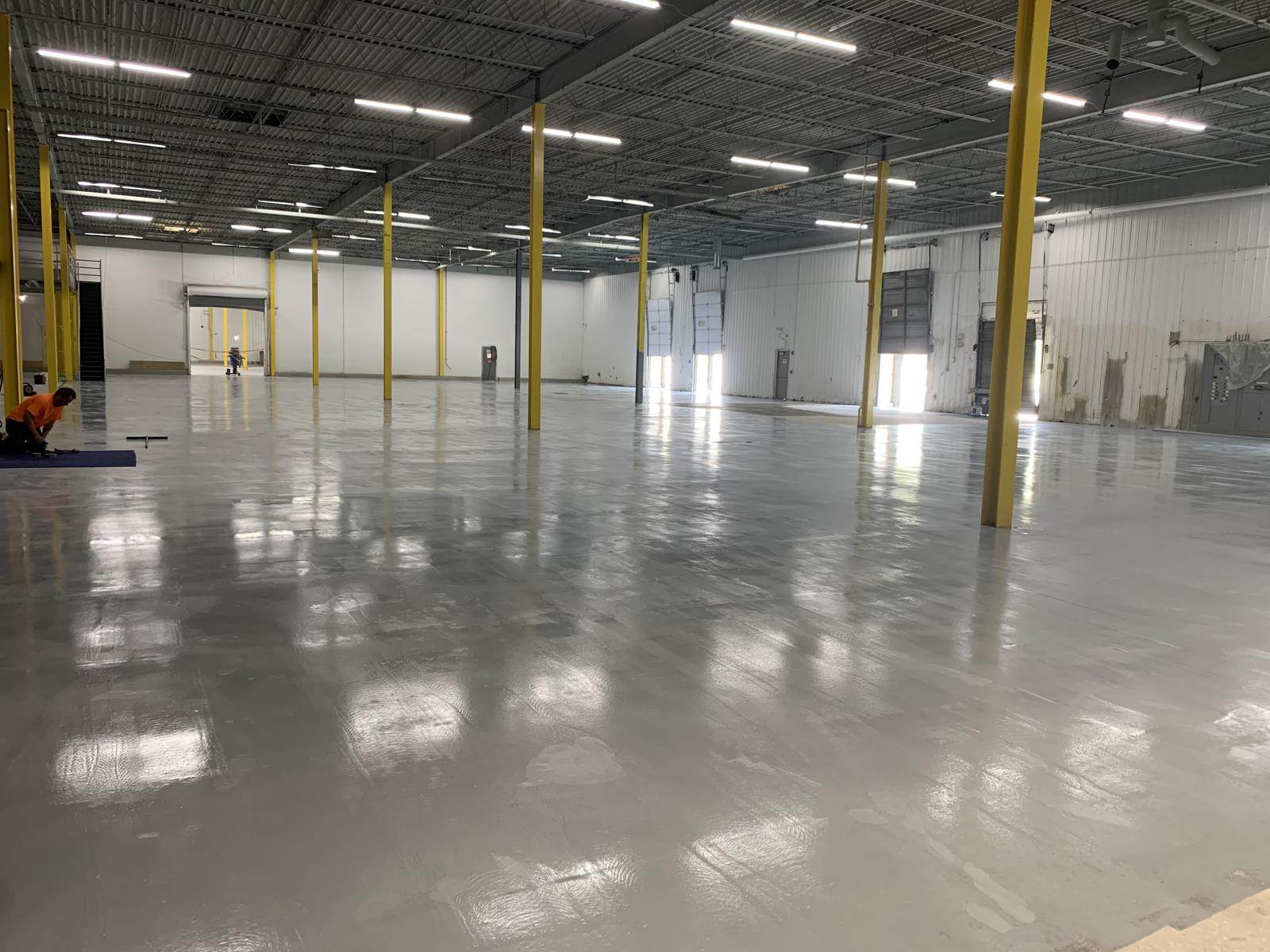 Completed distribution floor with a sealed, reflective slab and rows of yellow-guarded columns running the length of the building