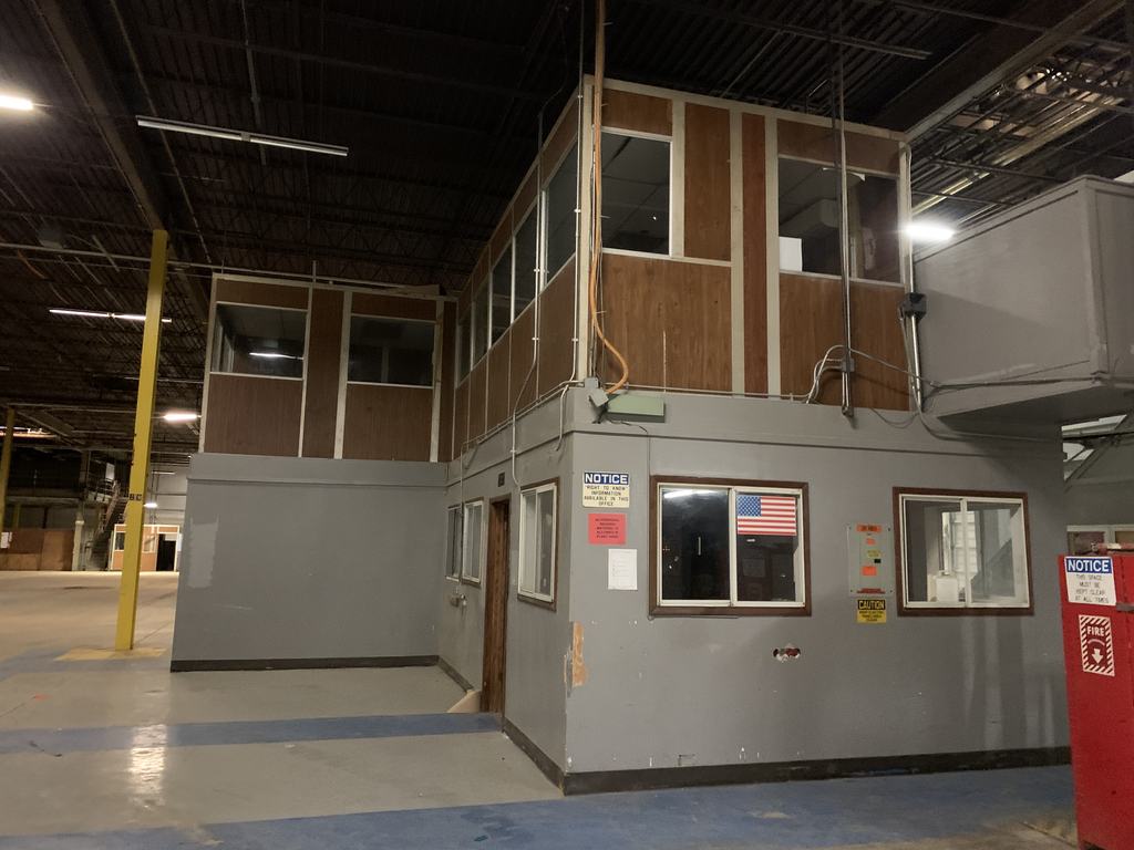 Two-story mezzanine office structure standing on the warehouse floor before demolition, with windowed offices on both levels