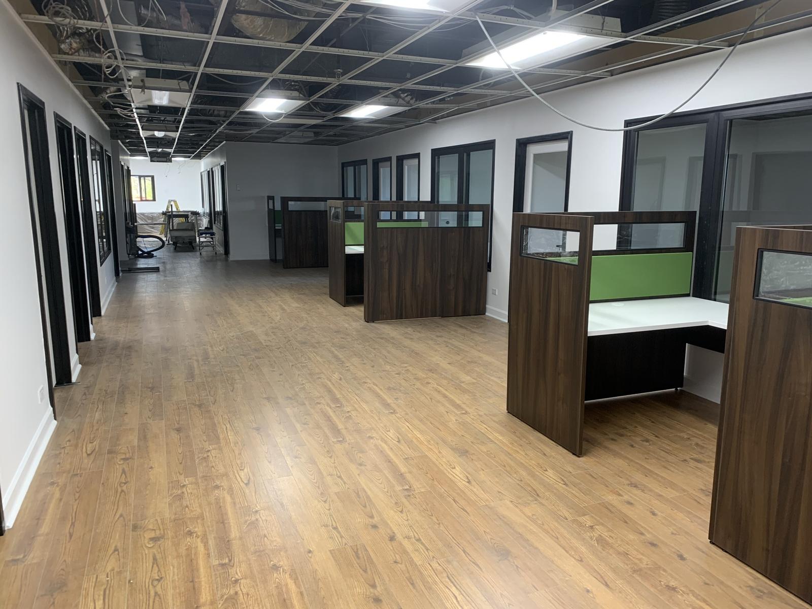 Renovated office area with new wood-look flooring, glazed partitions, and workstations along the corridor