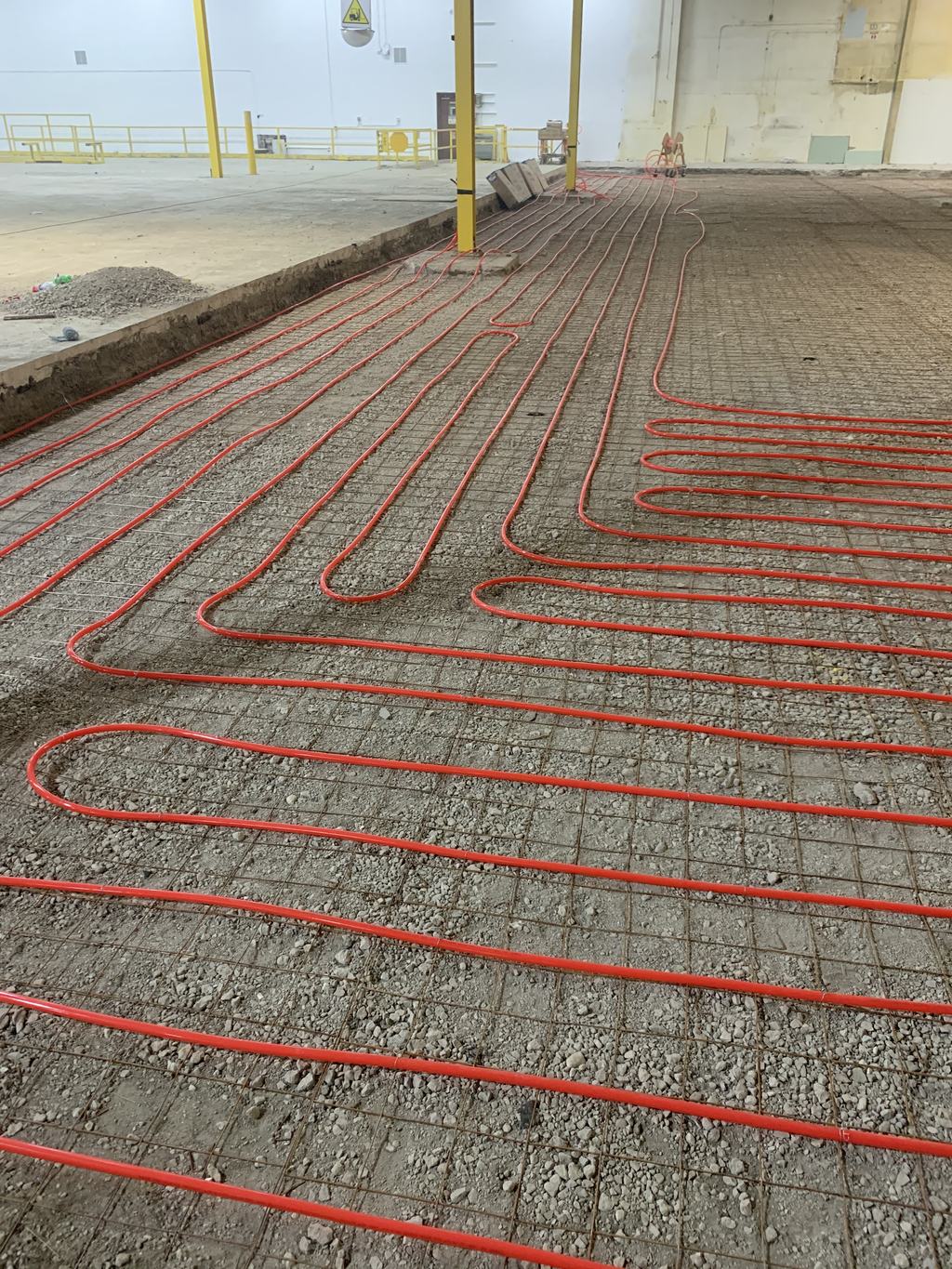 Loops of tubing tied to reinforcing mesh over the stone base, ready for the slab pour